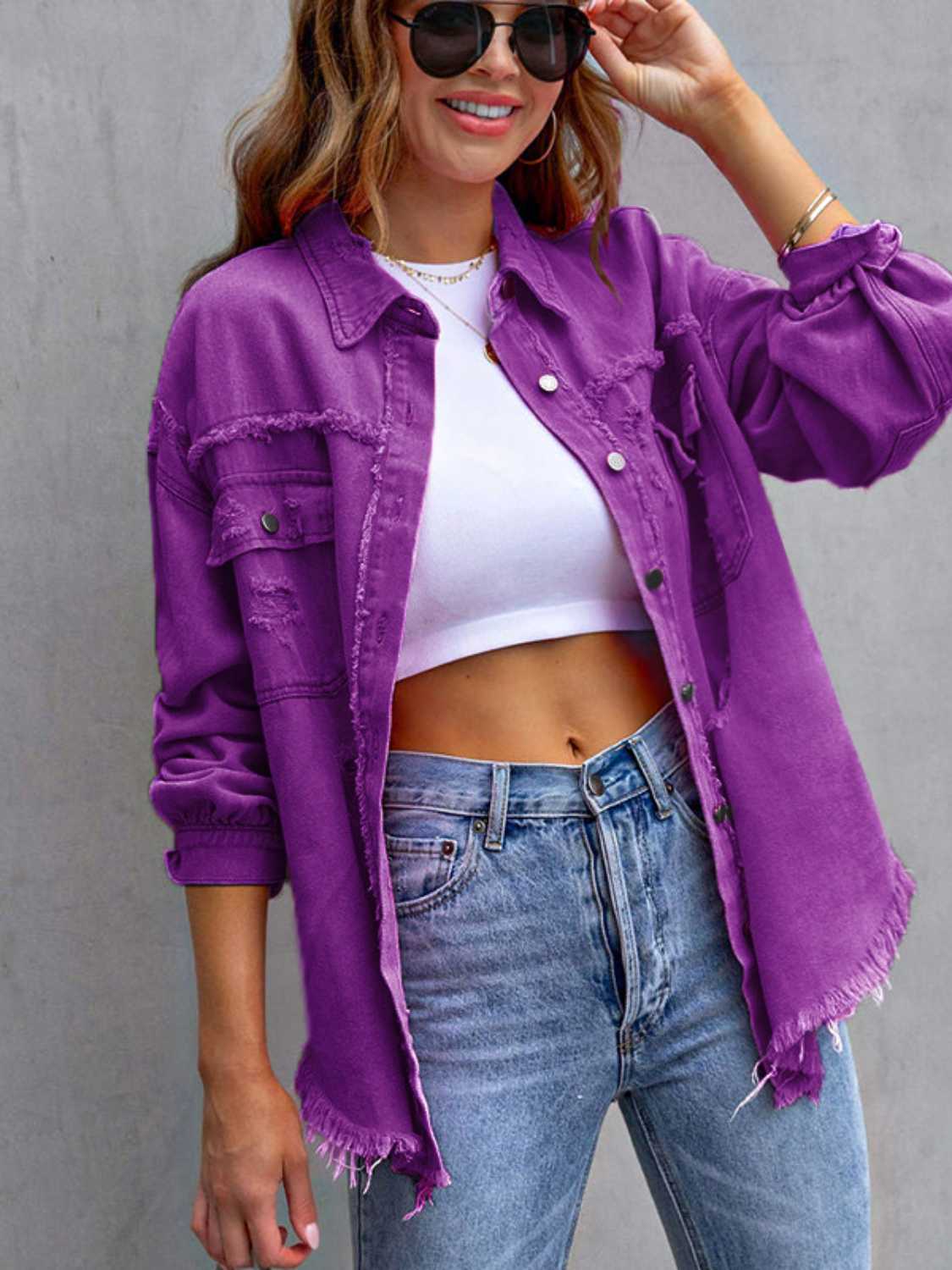 Woman wearing a purple distressed drop shoulder denim jacket with fringe trim over a white crop top.