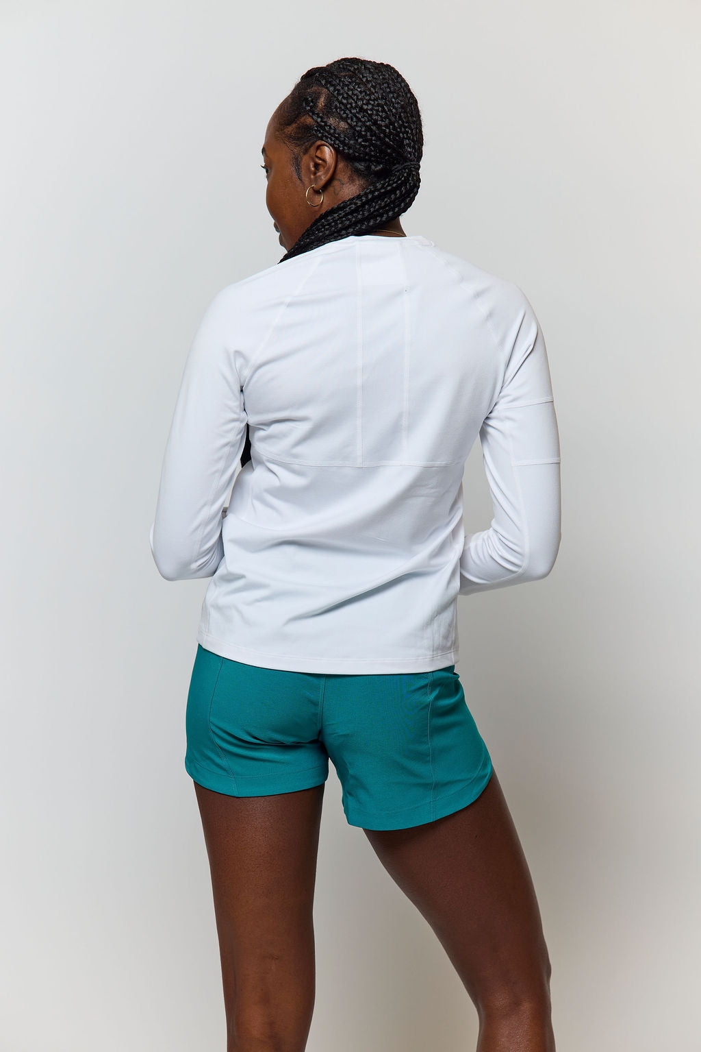 Woman from behind wearing white long-sleeve shirt and teal workout shorts.