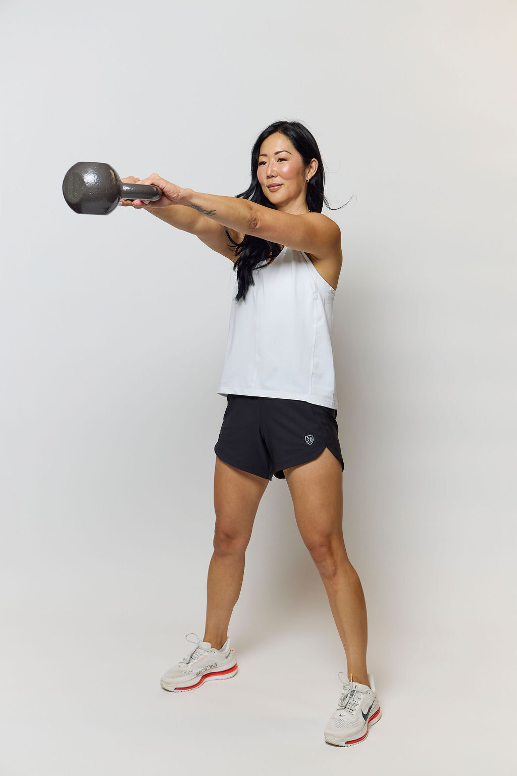 Woman in white tank top and black Goal Five Excel workout shorts holding a kettlebell.