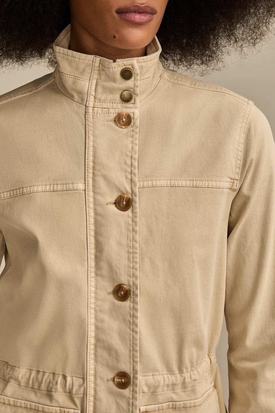 Close-up of a woman wearing a tan utility jacket with buttons and stitching details.