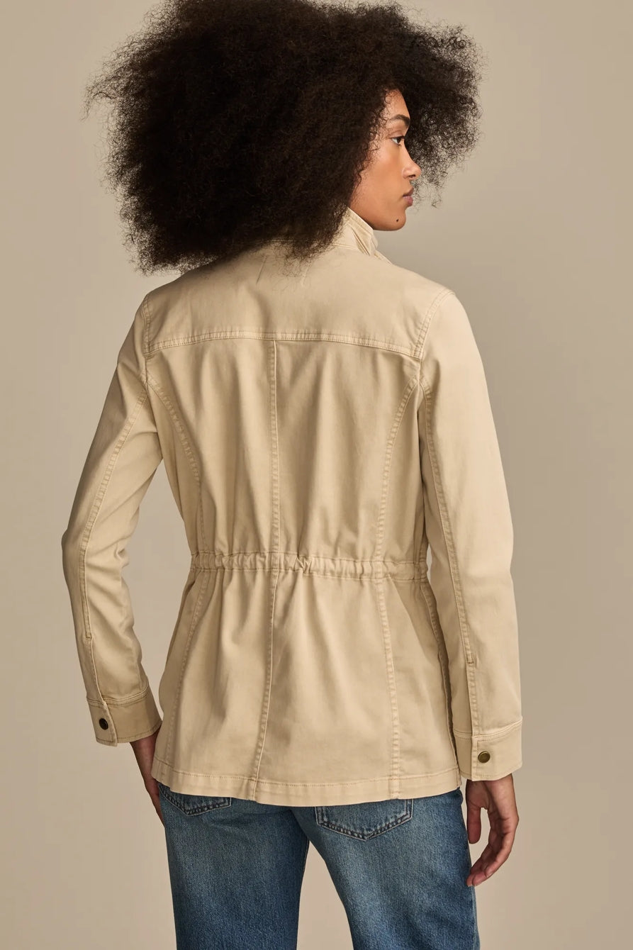 Back view of a woman wearing a tan Lucky Brand utility jacket and blue jeans.