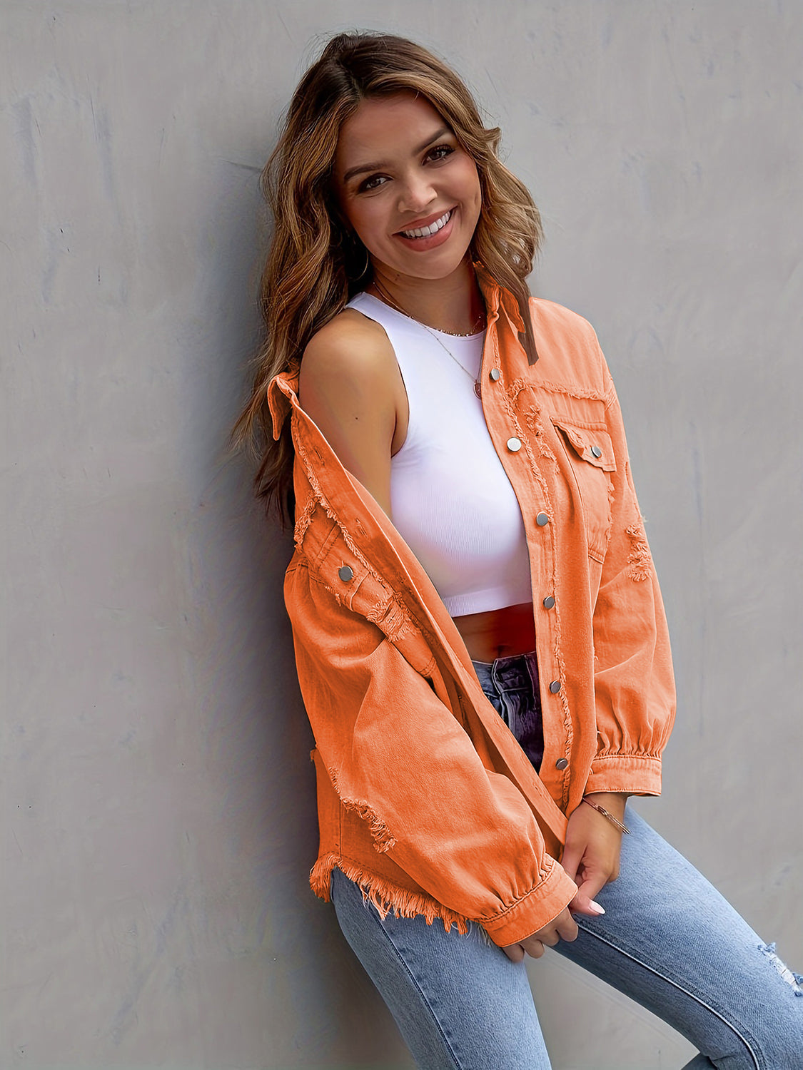 Woman wearing an orange distressed drop shoulder denim jacket with fringe trim and silver buttons.