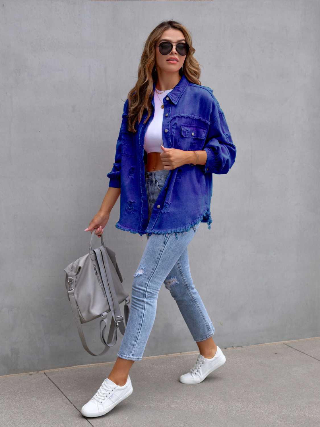 Woman wearing a blue distressed drop shoulder denim jacket with fringe hem and ripped details.