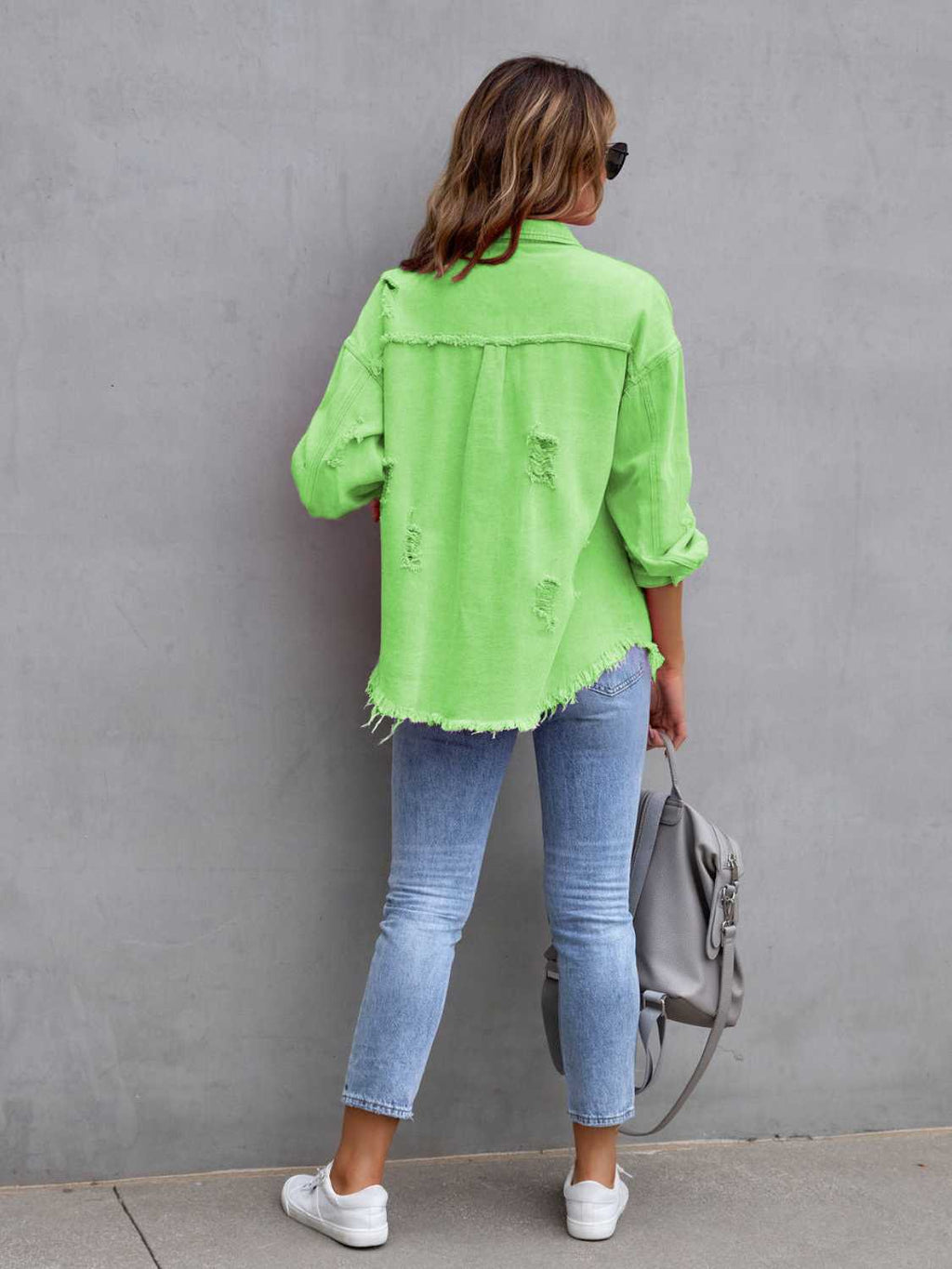 Back view of a lime green distressed drop shoulder denim jacket with fringe hem and ripped details.