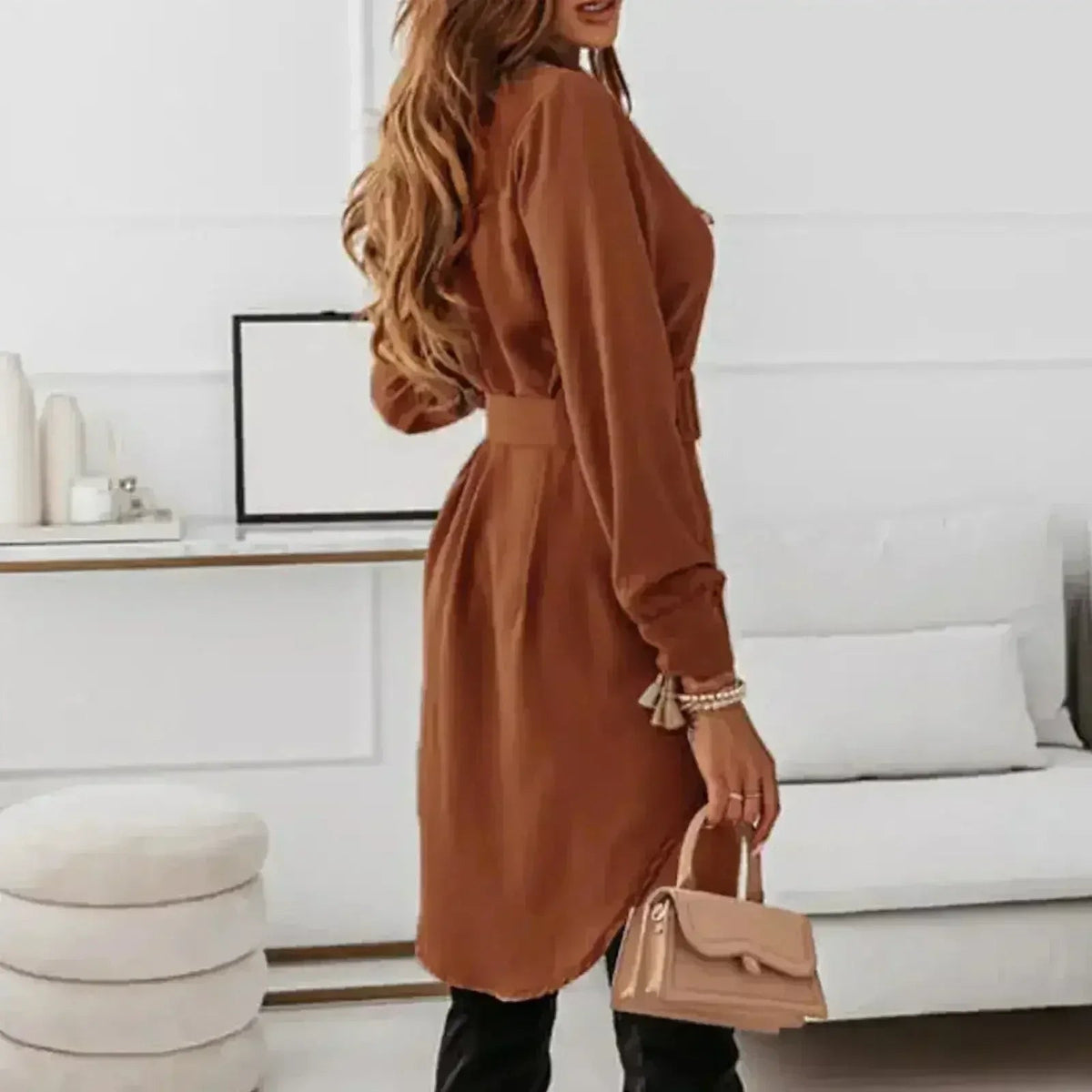 Woman wearing a brown A-line shirt dress with a belt and black pants, holding a beige handbag.