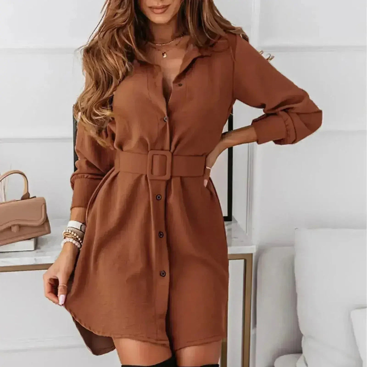 Woman wearing a brown A-line shirt dress with a belt and long sleeves.