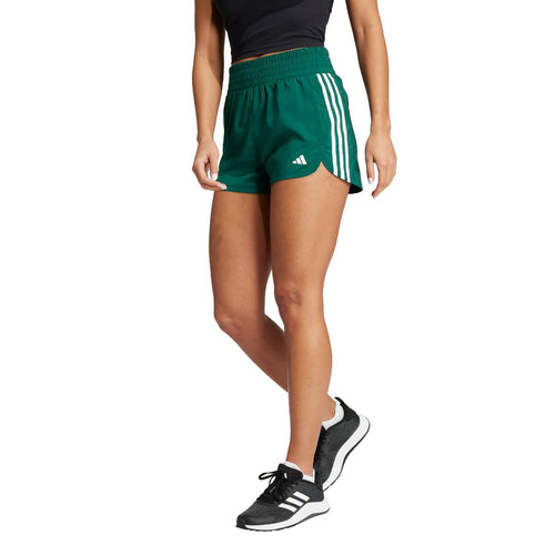 Woman wearing green Adidas Pacer 3-Stripes high-rise woven training shorts and black sneakers.