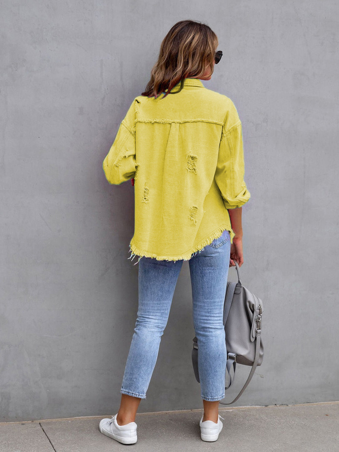 Back view of a yellow distressed drop shoulder denim jacket with fringe hem and ripped details.
