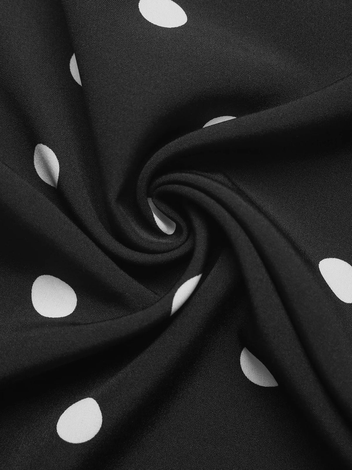 Close-up of black fabric with white polka dots, showing a soft, swirled texture.