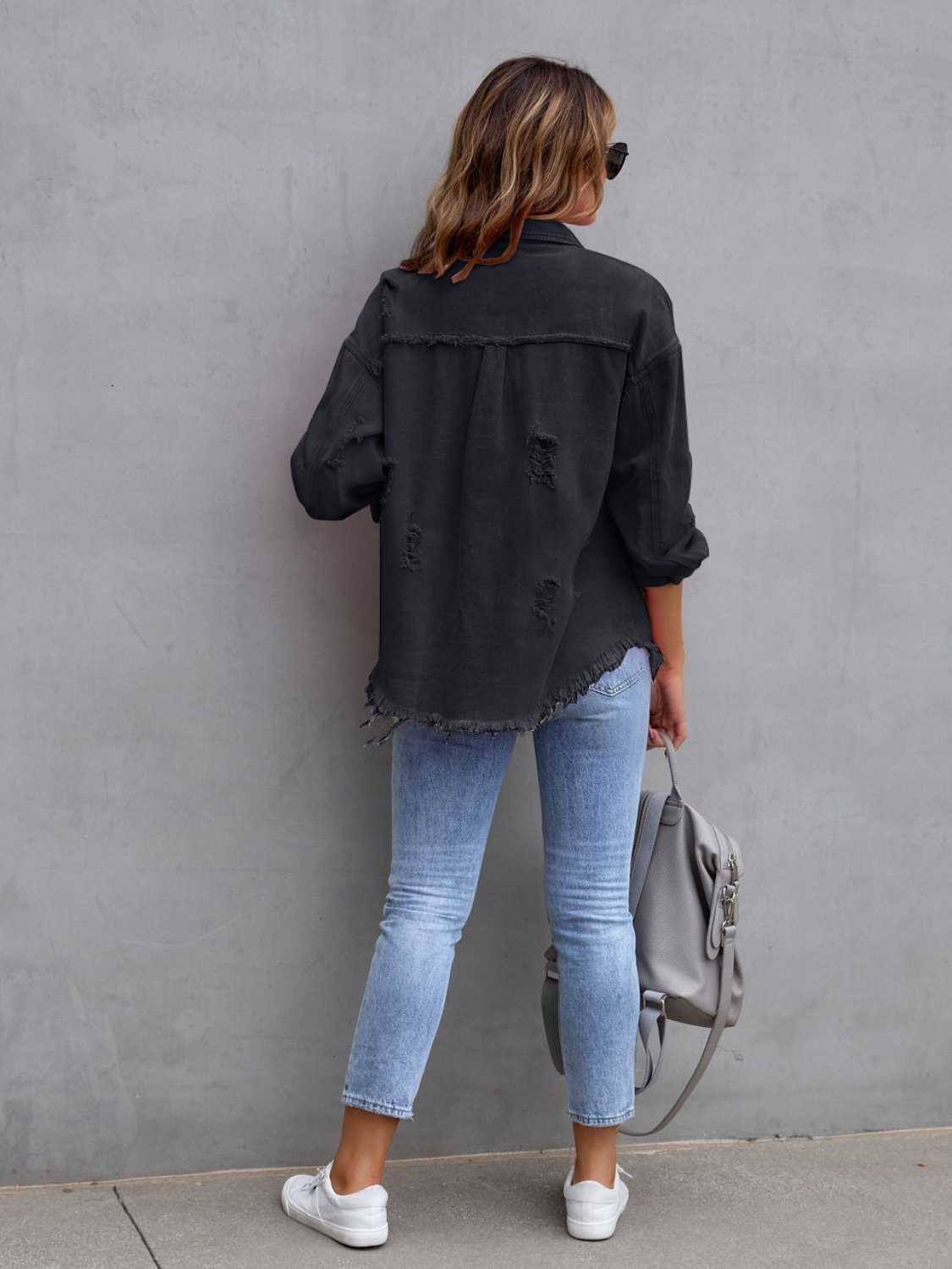 Back view of a black distressed drop shoulder denim jacket with fringe hem and ripped details.