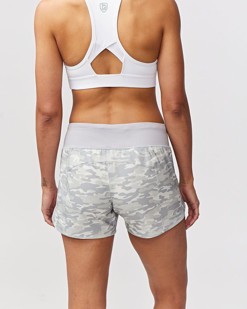 Back view of a woman wearing white sports bra and grey camouflage print workout shorts with a hidden pocket.