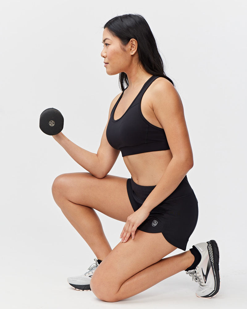 Woman in black workout shorts and sports bra holding a dumbbell.