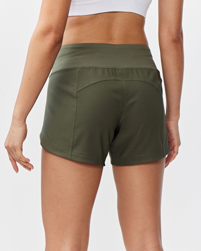 Back view of a woman wearing dark moss green Goal Five Excel women's workout shorts.