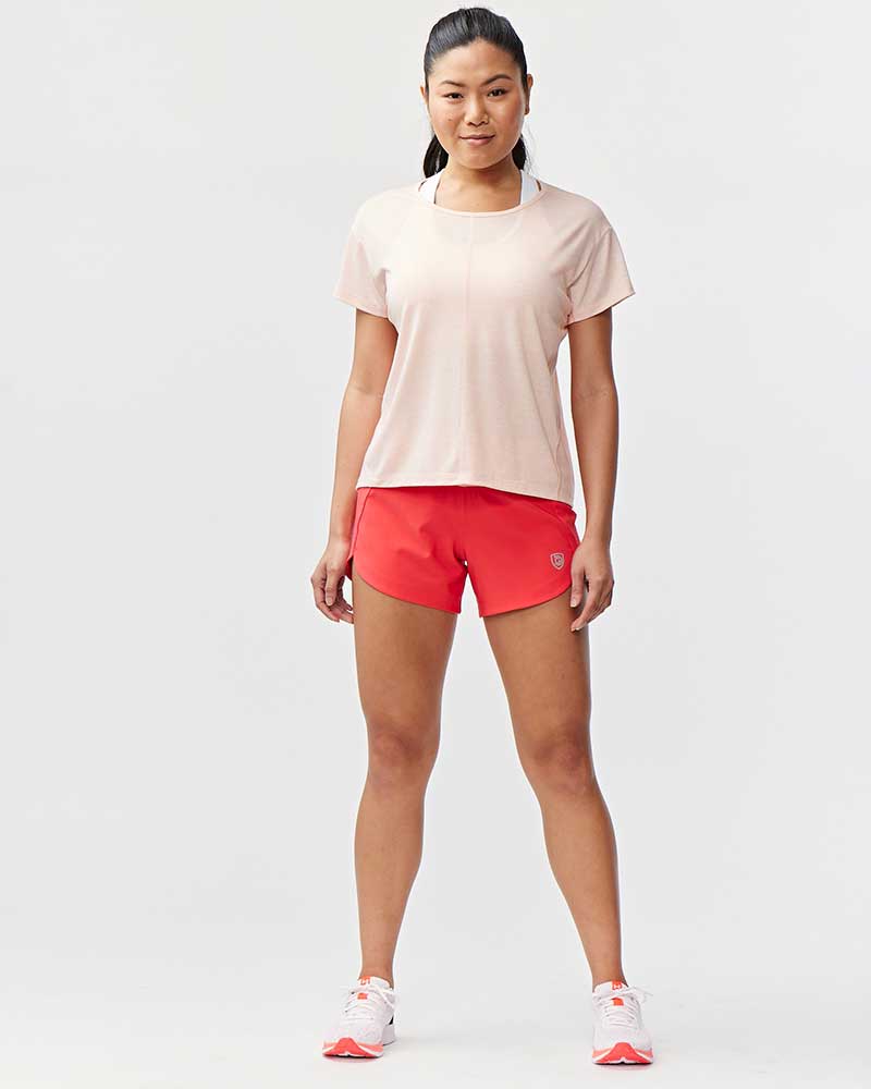 Woman wearing coral workout shorts and a light pink t-shirt, standing against a white background.