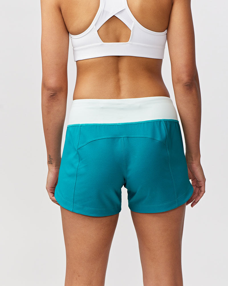 Back view of a woman wearing teal Goal Five Excel workout shorts with a white waistband.