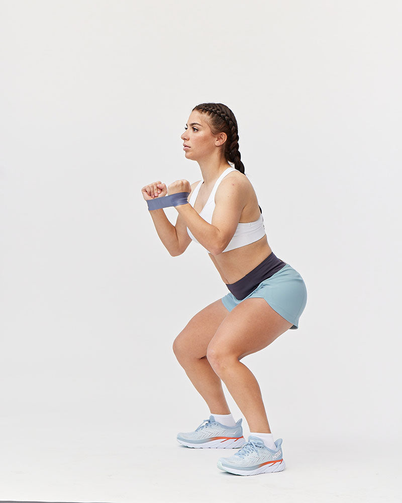 Woman wearing Goal Five Excel Women's Workout Shorts in mineral blue during a squat exercise.