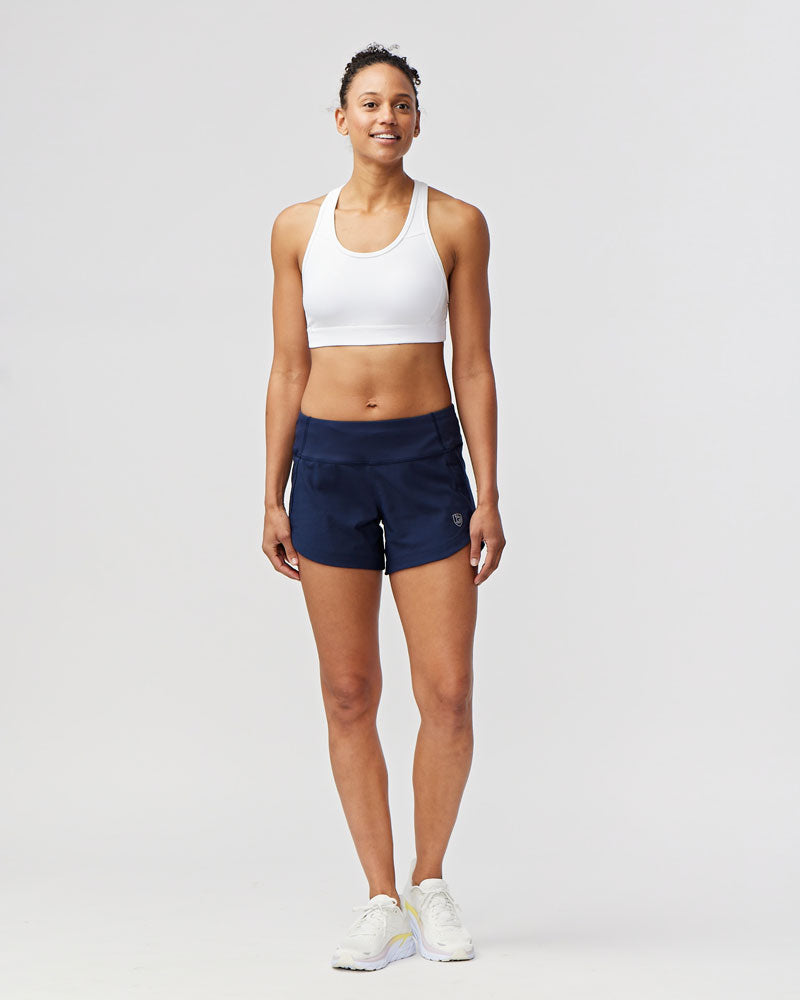 Woman wearing navy blue Goal Five Excel workout shorts and a white sports bra.