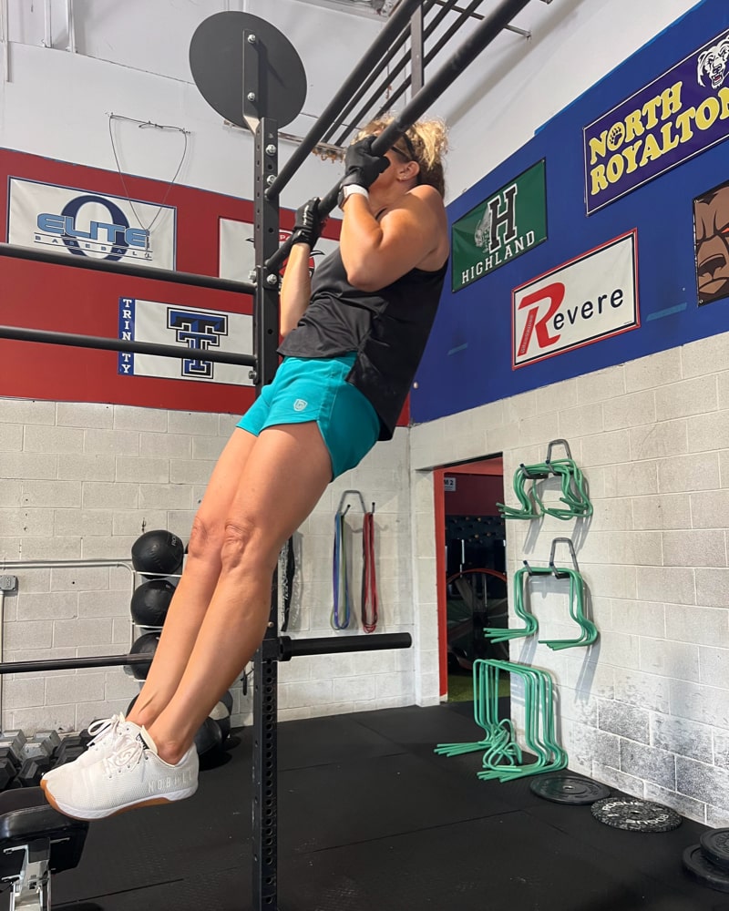 Woman performing a pull-up in teal Goal Five Excel workout shorts with a hidden pocket.