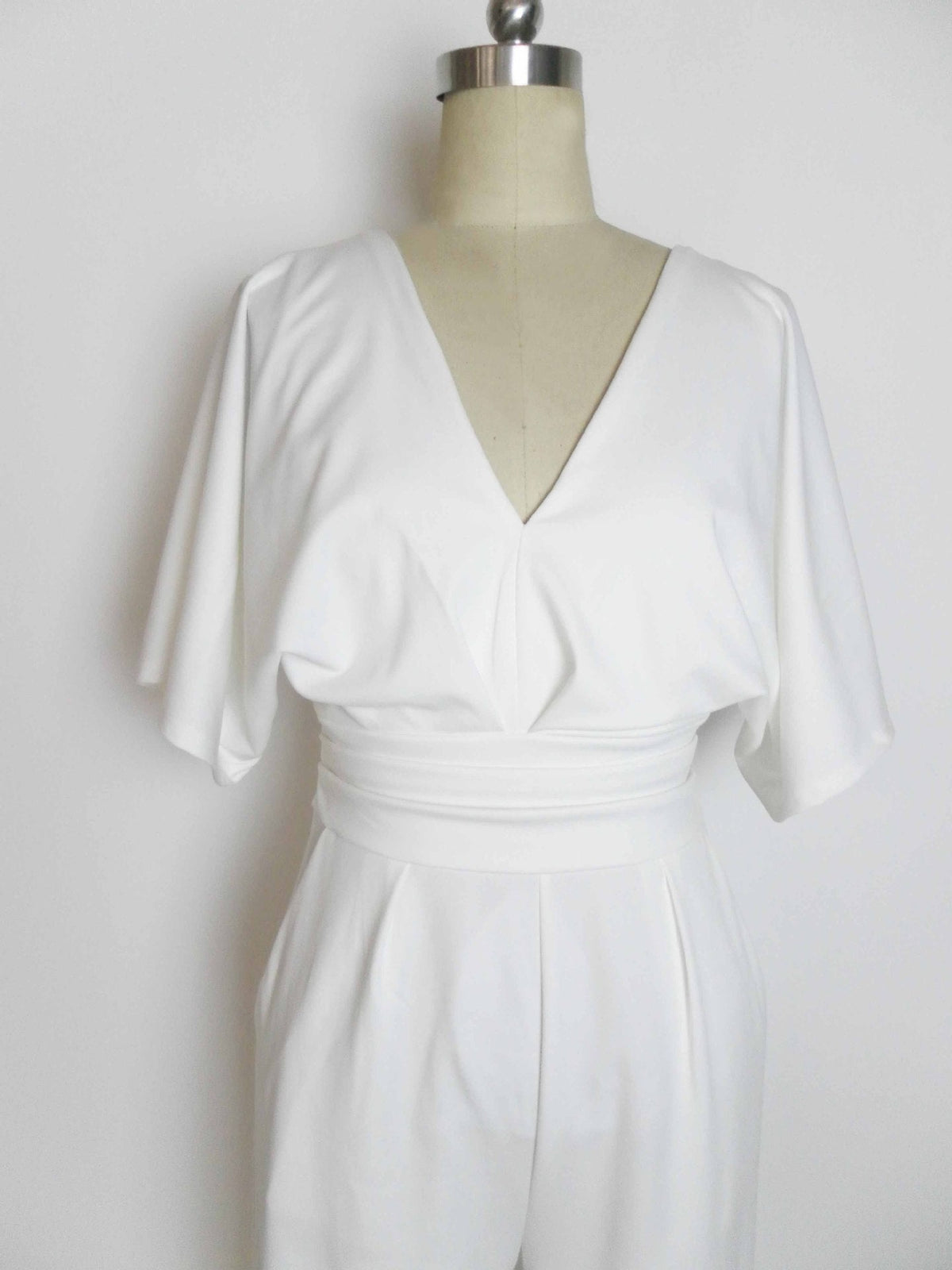 White wide-leg jumpsuit with a deep V-neck and a cinched waist, displayed on a mannequin.