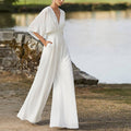 Woman wearing a white wide-leg jumpsuit with a deep V-neck and cinched waist.