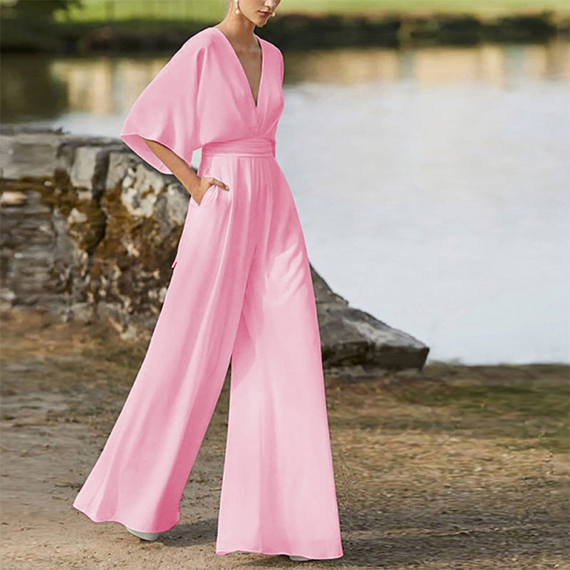 Pink wide leg jumpsuit with a deep V-neck and belted waist, worn by a model outdoors.