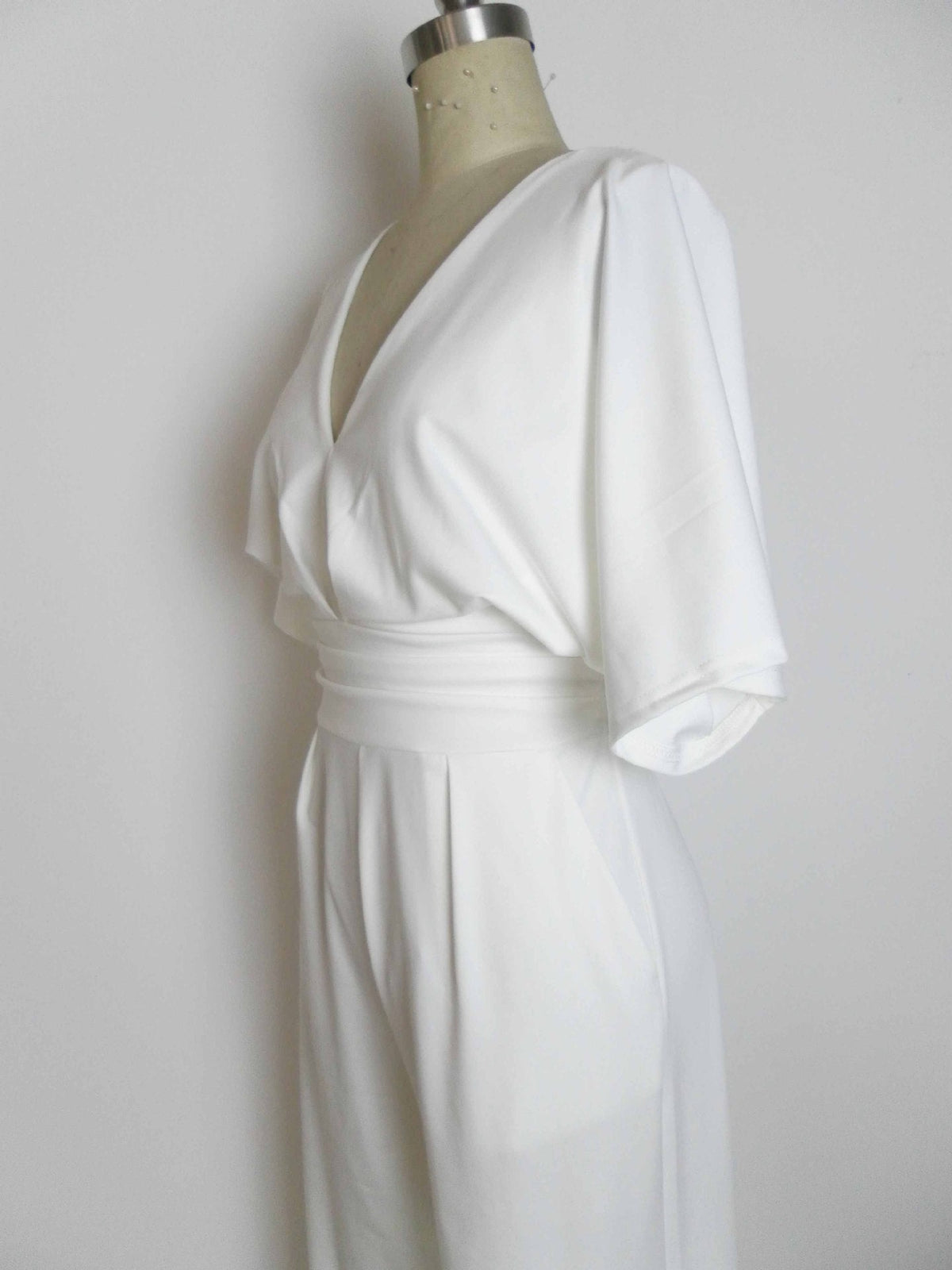 White wide-leg jumpsuit with a deep V-neck and a cinched waist, displayed on a mannequin.