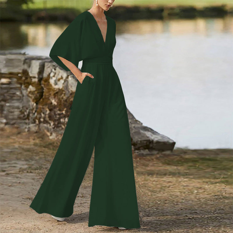 Woman wearing a dark green wide-leg jumpsuit with a deep V-neck and short sleeves, standing outdoors.