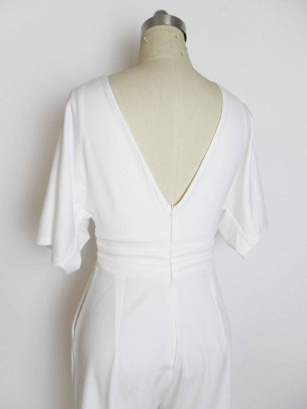 Back view of a white M.ZX Wide Leg Jumpsuit on a mannequin, featuring a deep V-neck and zipper closure.