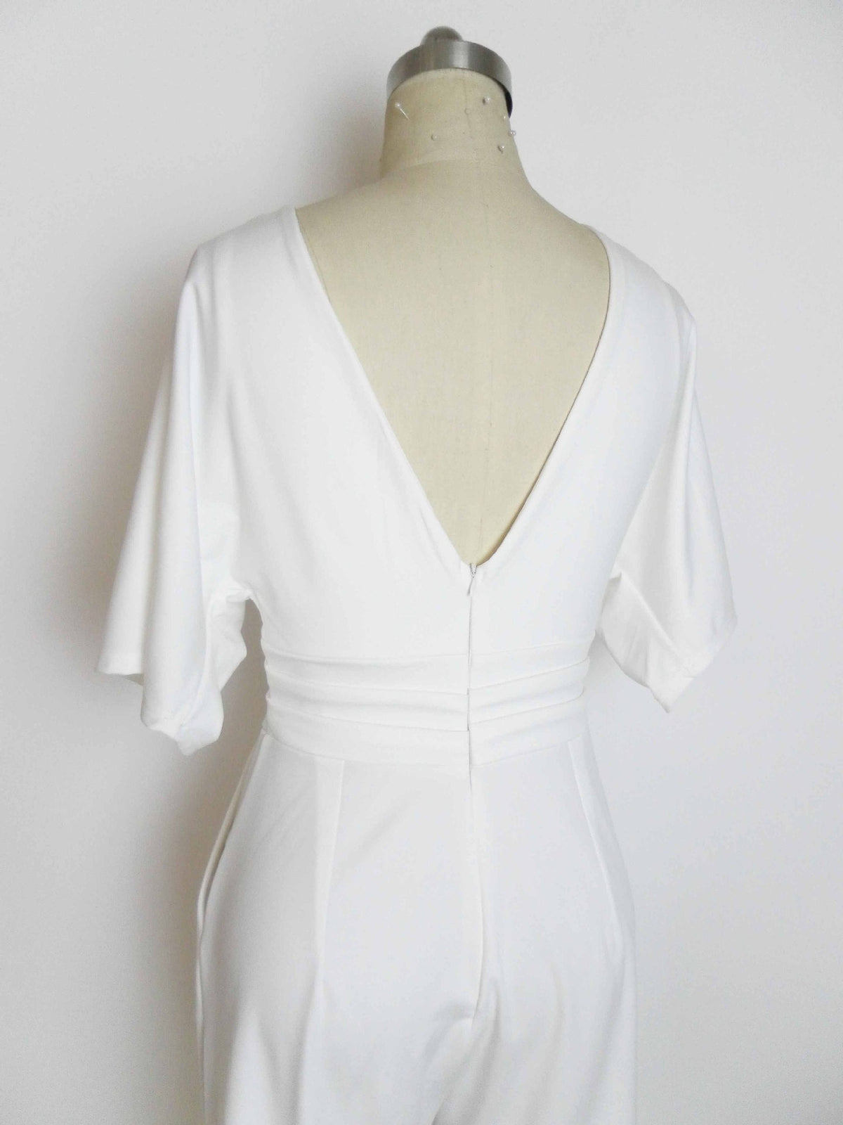 Back view of a white M.ZX Wide Leg Jumpsuit on a mannequin, featuring a deep V-neck and zipper closure.
