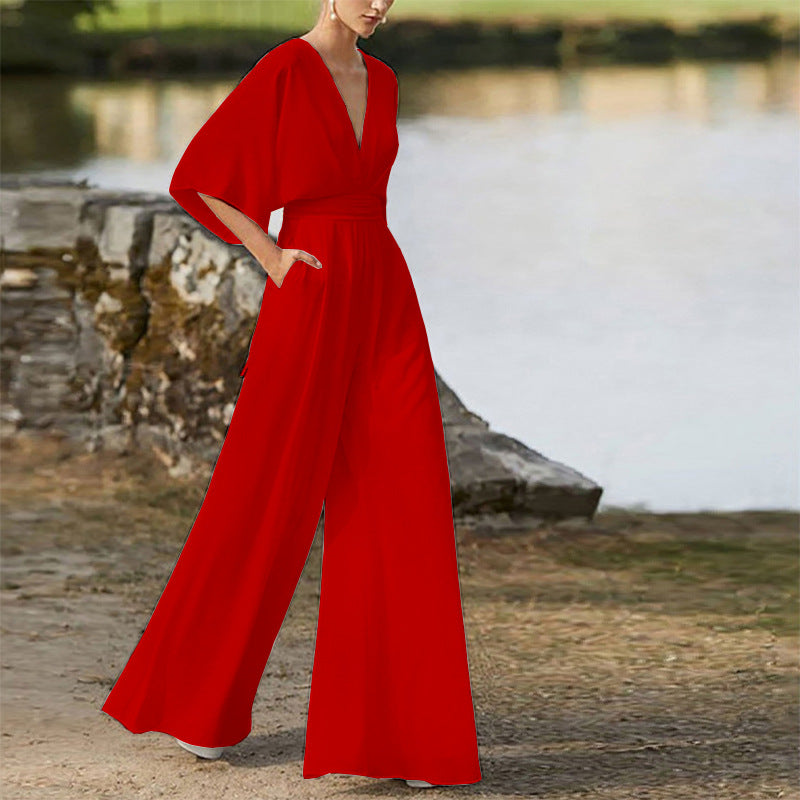 Red wide leg jumpsuit with deep V-neck and short sleeves, worn by a woman outdoors.