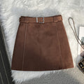 Brown suede A-line mini skirt with a high waist and matching belt on a white faux fur background.