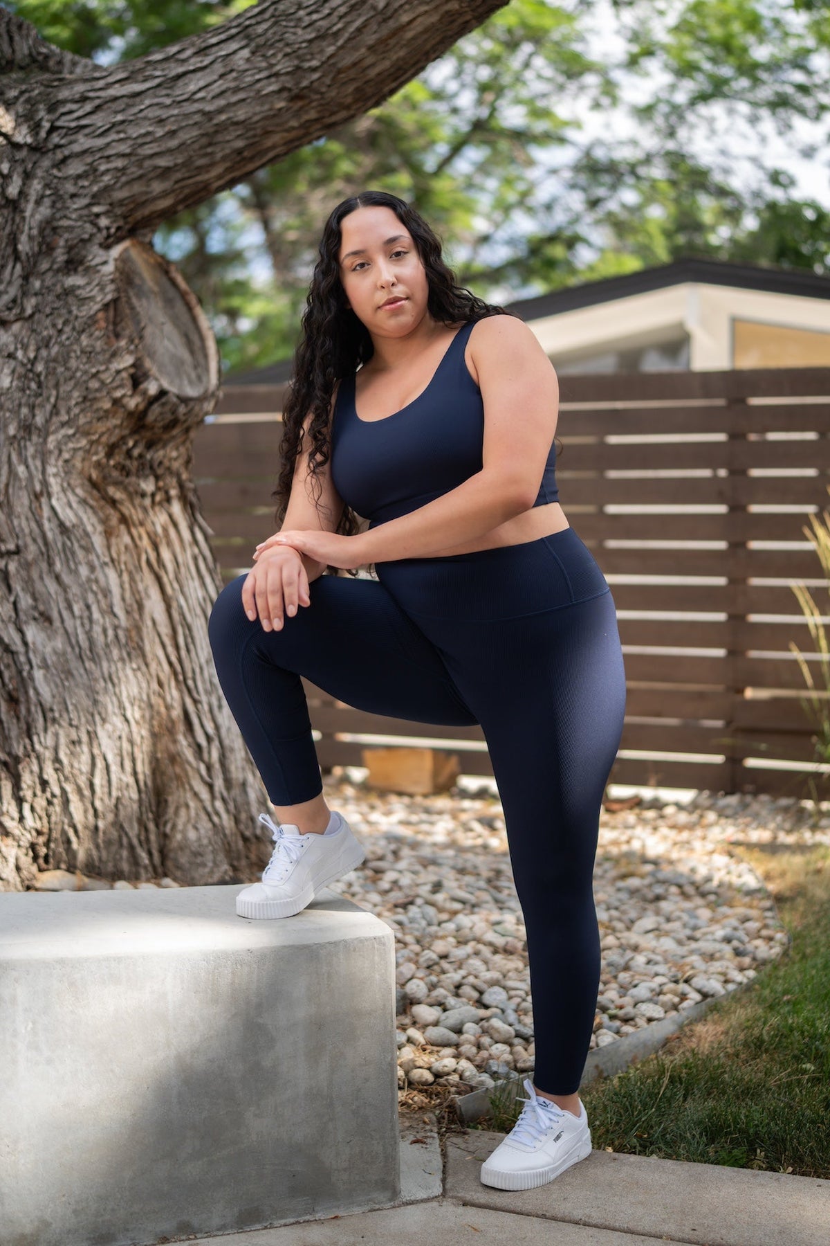 Woman wearing navy blue high-rise ribbed leggings and a matching sports bra with white sneakers.