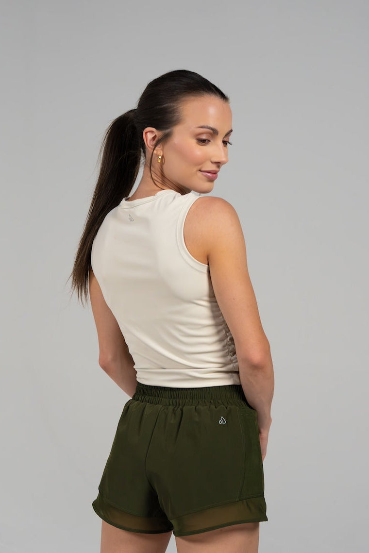 Back view of a woman wearing the GRAVITY soaring tank in muslin with olive green athletic shorts.