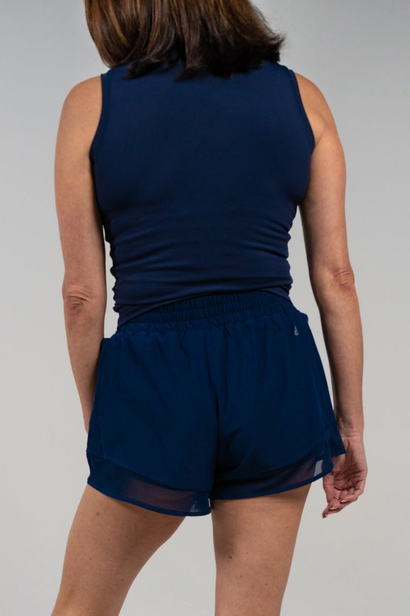 Back view of a woman wearing a navy blue GRAVITY soaring tank and matching athletic shorts.