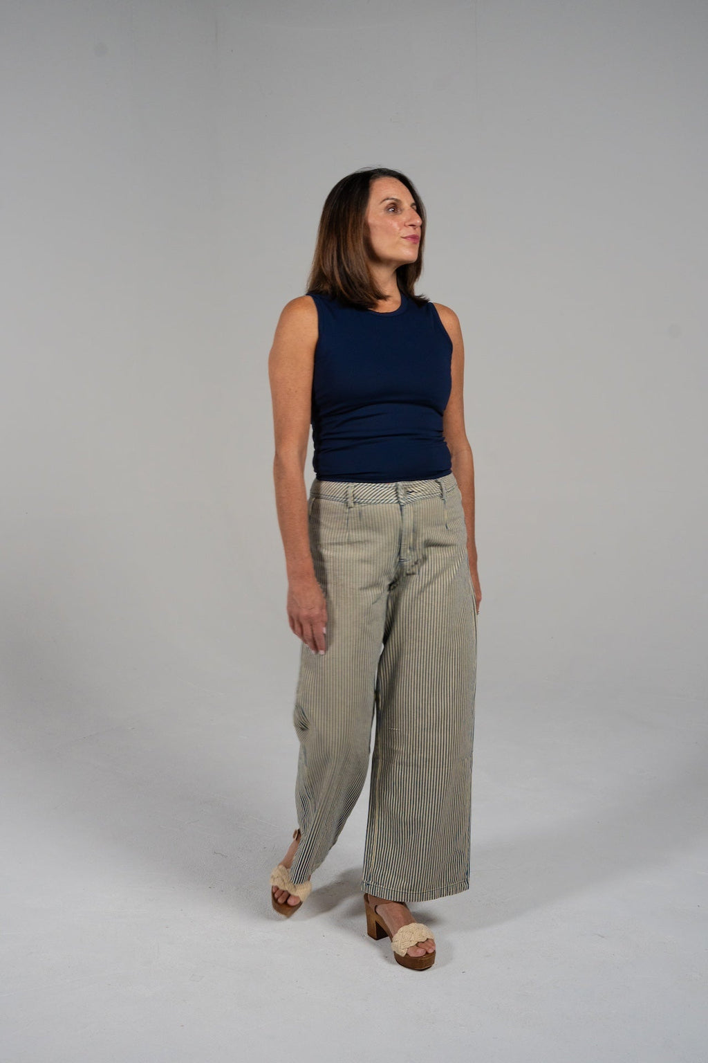 Woman wearing a navy GRAVITY soaring tank with synched sides and striped wide-leg pants.
