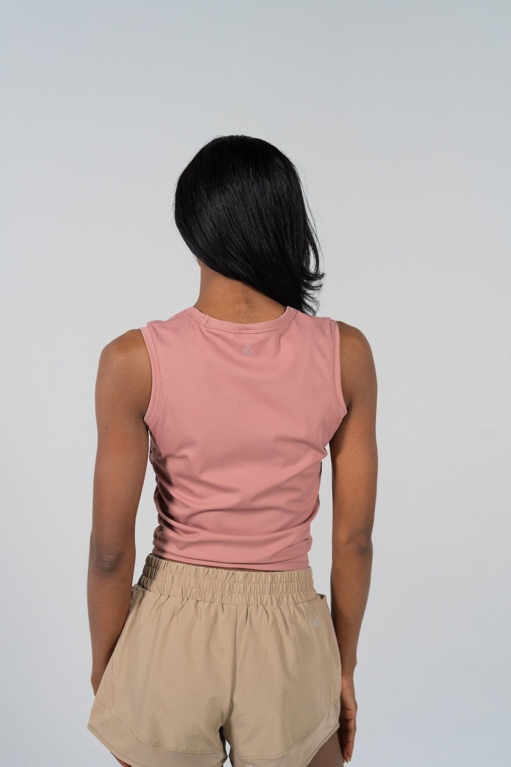 Back view of a woman wearing a slim-fit, waist-length pink GRAVITY soaring tank and tan shorts.