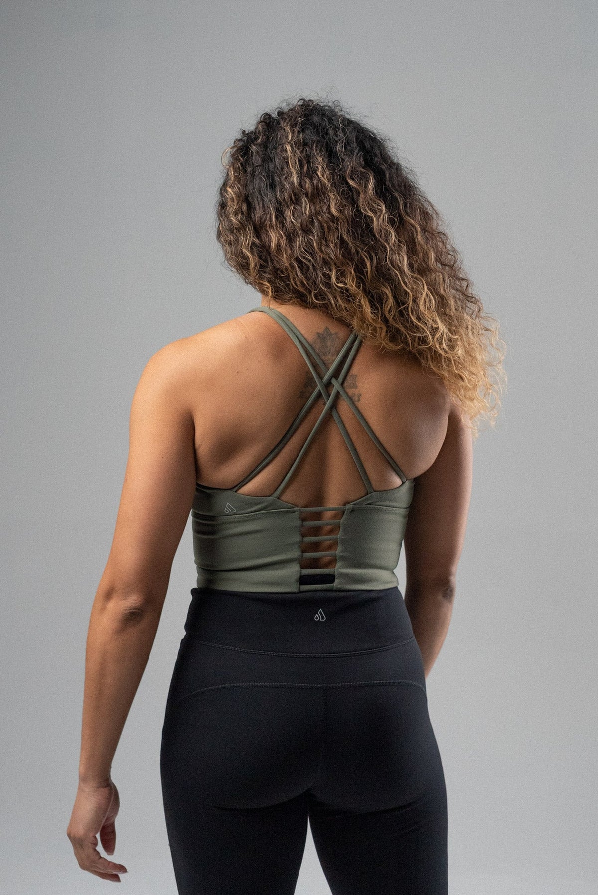 Back view of a woman wearing a green Alyth Active crop bra with black leggings.