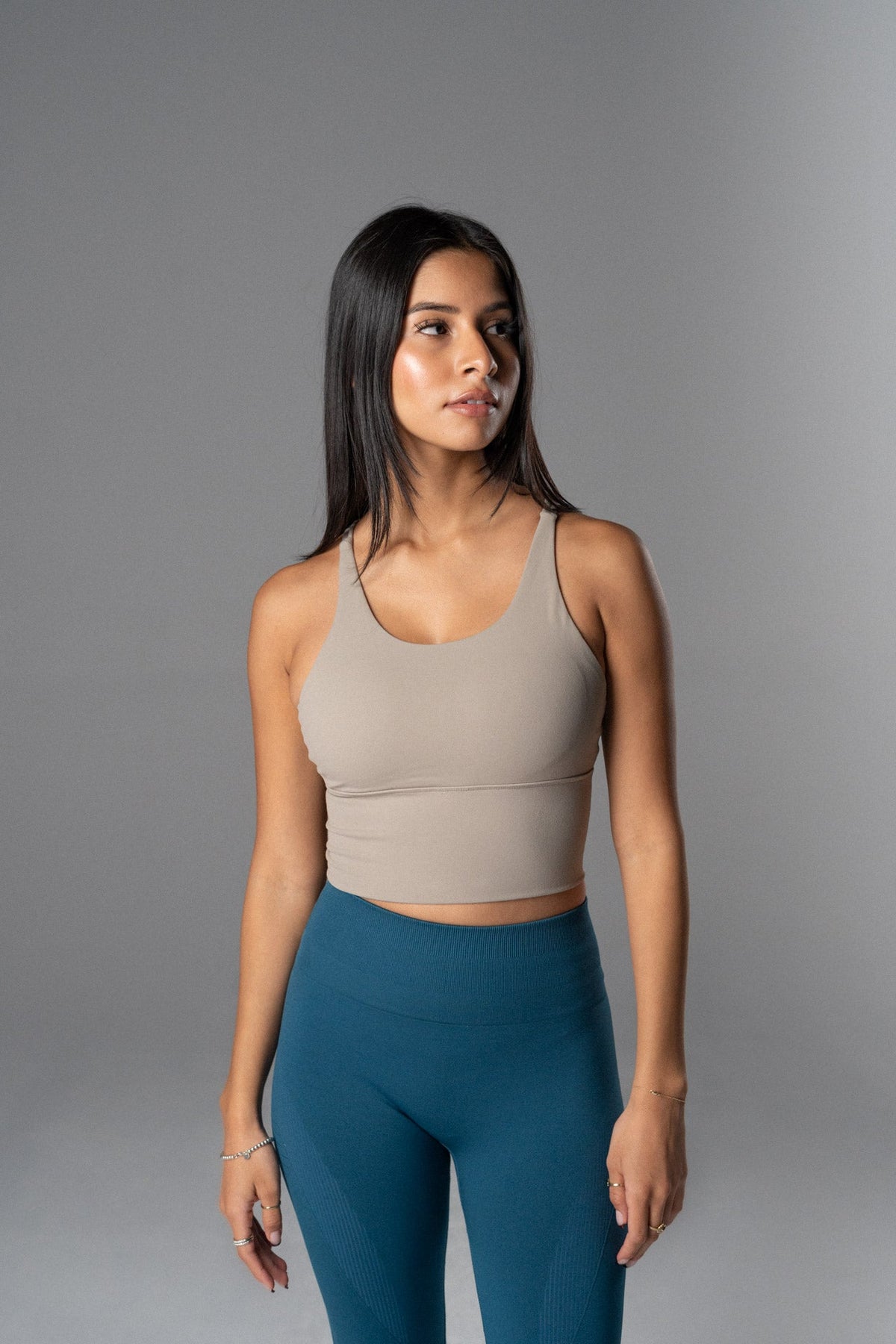 Woman wearing a beige Alyth Active Rebellious High Impact Crop Bra and blue leggings.