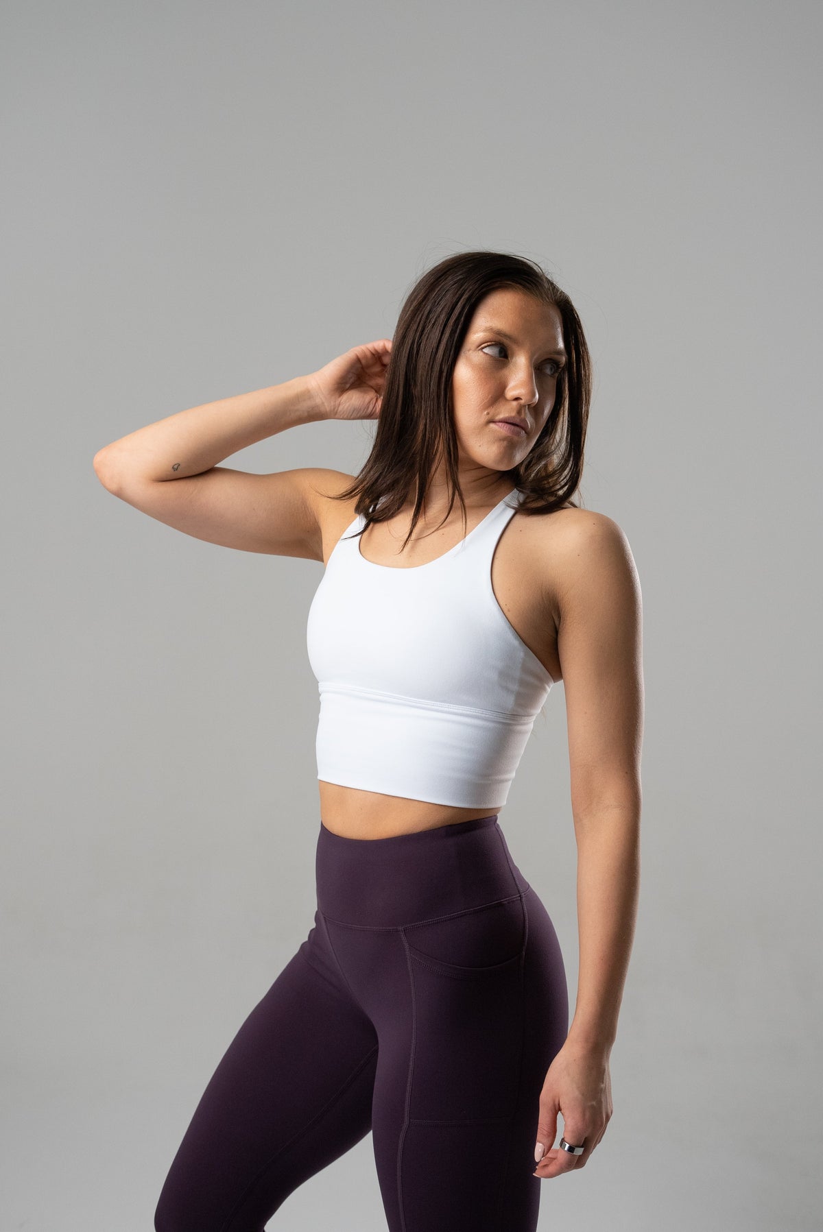 Woman wearing a white Alyth Active Rebellious High Impact Crop Bra with removable pads and dark purple leggings.