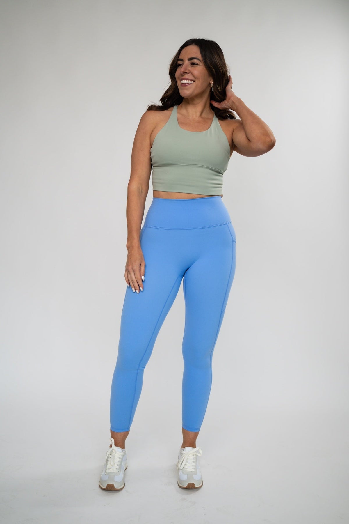 Woman wearing a sage green Alyth Active Rebellious high impact crop bra and blue leggings.