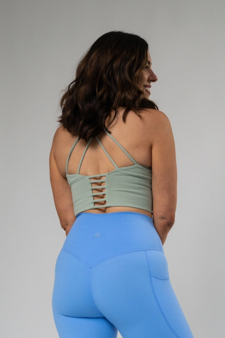 Woman from behind wearing a light green high-impact crop bra with strappy back and blue leggings.