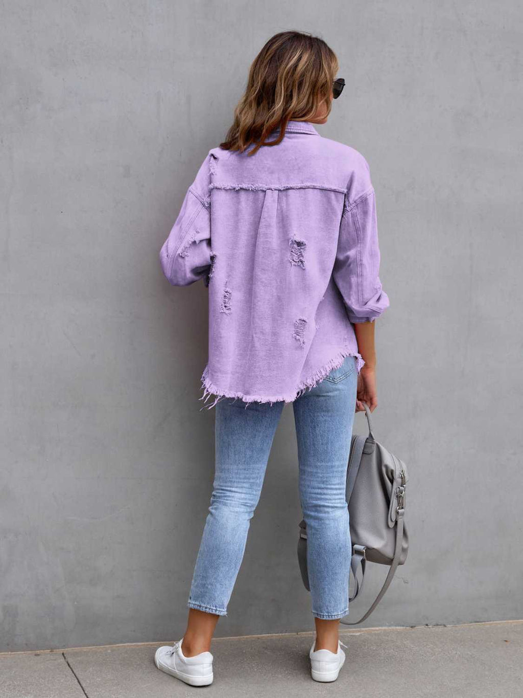 Back view of a woman wearing a purple distressed drop shoulder denim jacket with fringe hem.