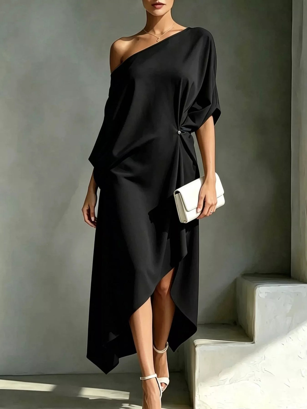 Plus size black asymmetrical one-shoulder drape dress with a white clutch and white heels.