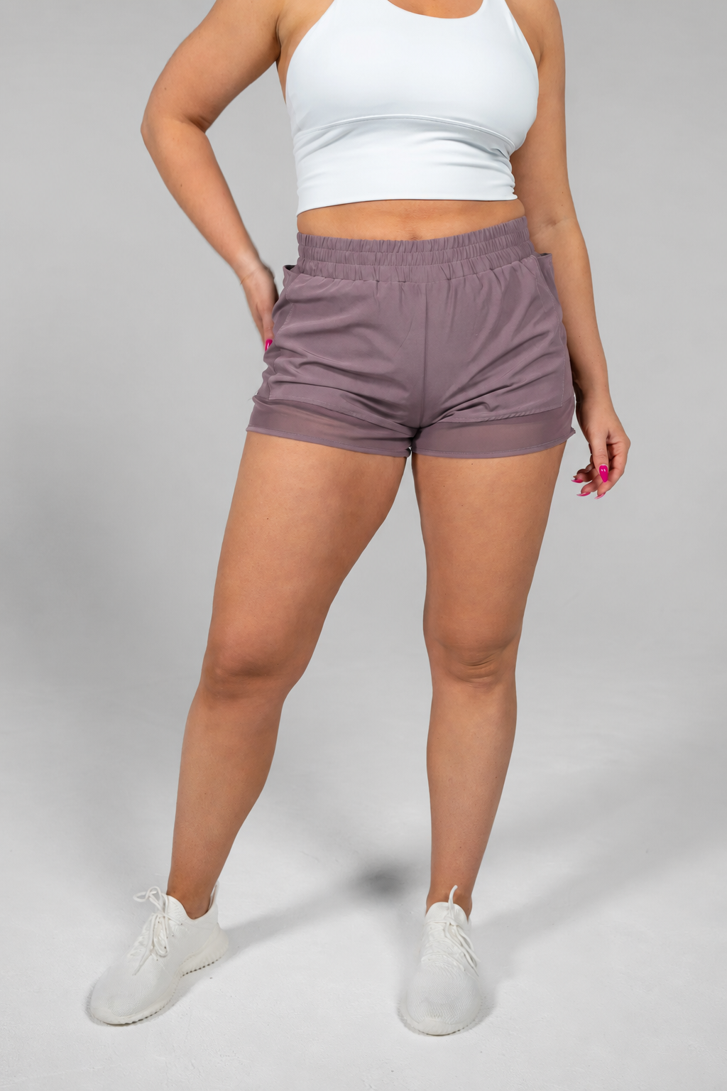 Woman wearing Alyth Active Empowered V3 Mid Rise Shorts in mauve with white sports bra and white sneakers.