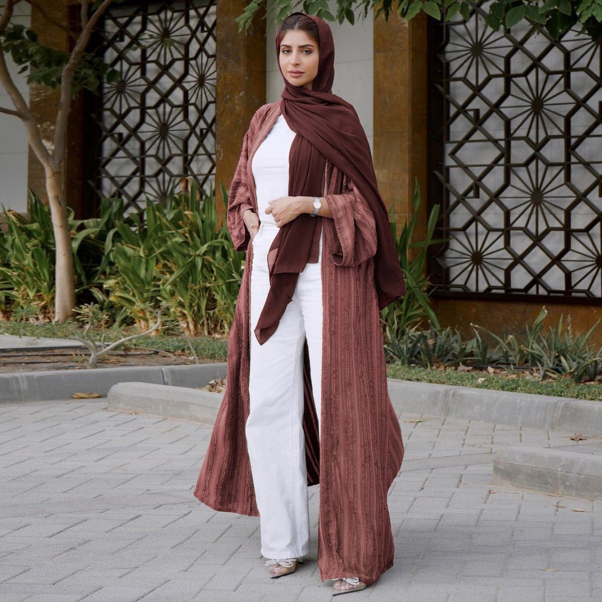 Woman wearing a vintage knitted longline open front cardigan abaya in mauve with white trousers.