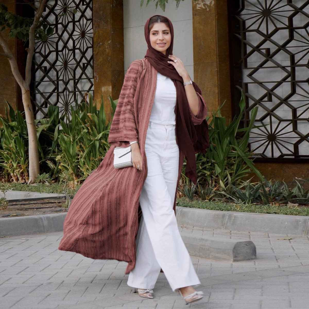Woman wearing a mauve vintage knitted longline open front cardigan abaya with white pants.