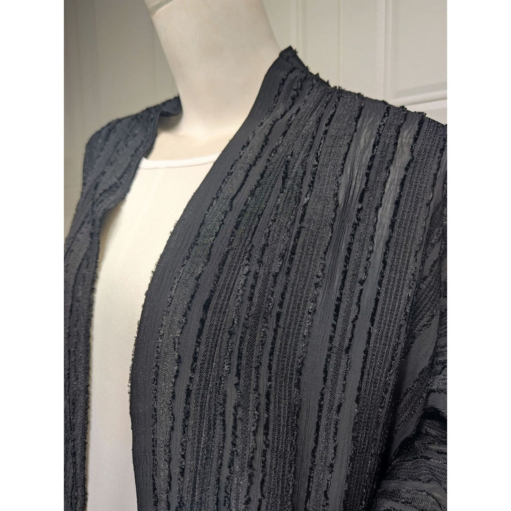 Close-up of a black textured knit open-front cardigan with vertical fringe details on a mannequin.