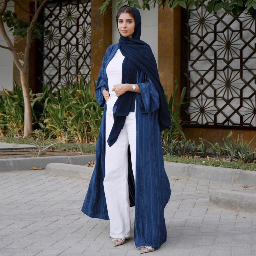 Woman wearing a navy blue vintage knitted longline open front cardigan abaya over white pants.