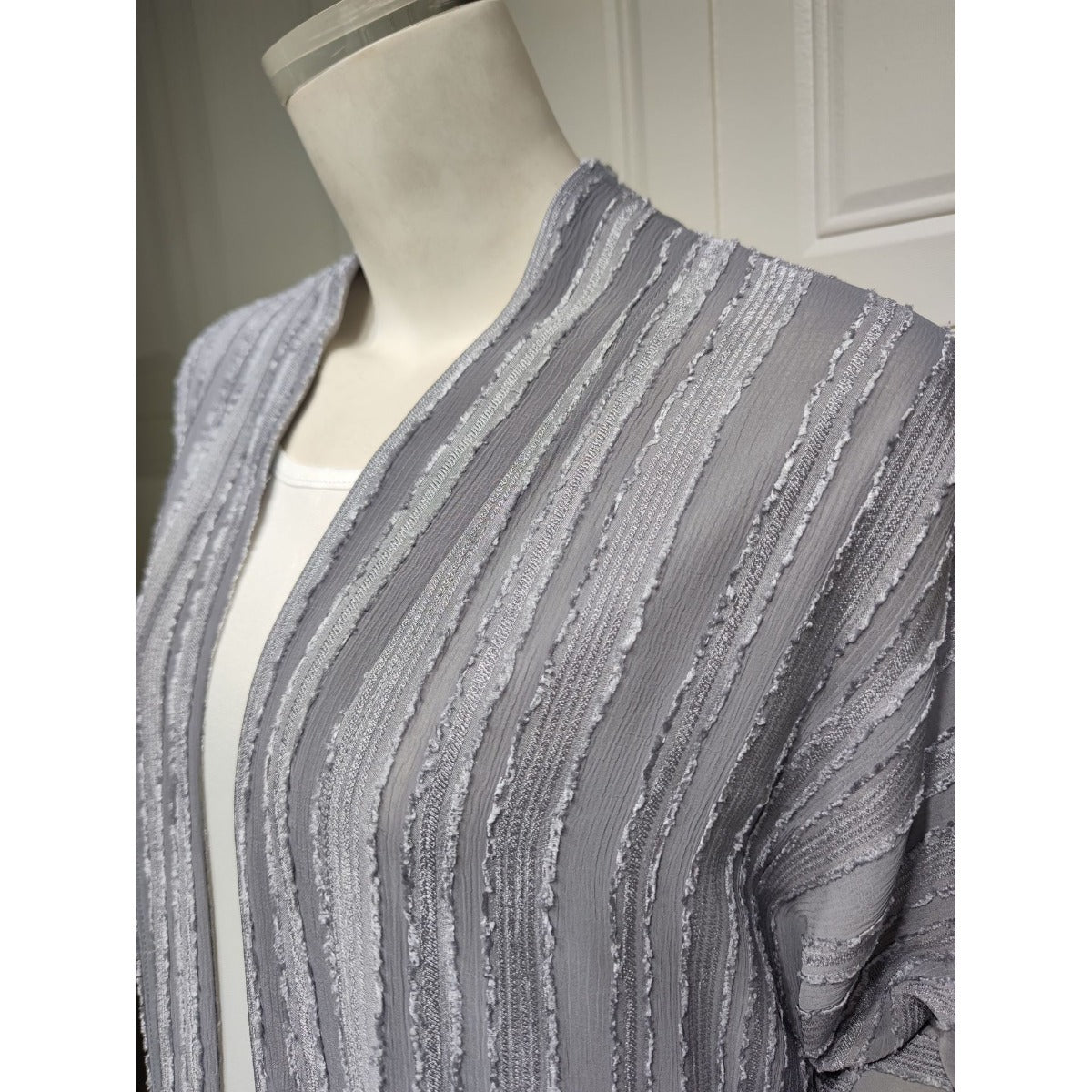 Close-up of a grey vintage knitted cardigan abaya with vertical stripes and fringe details.