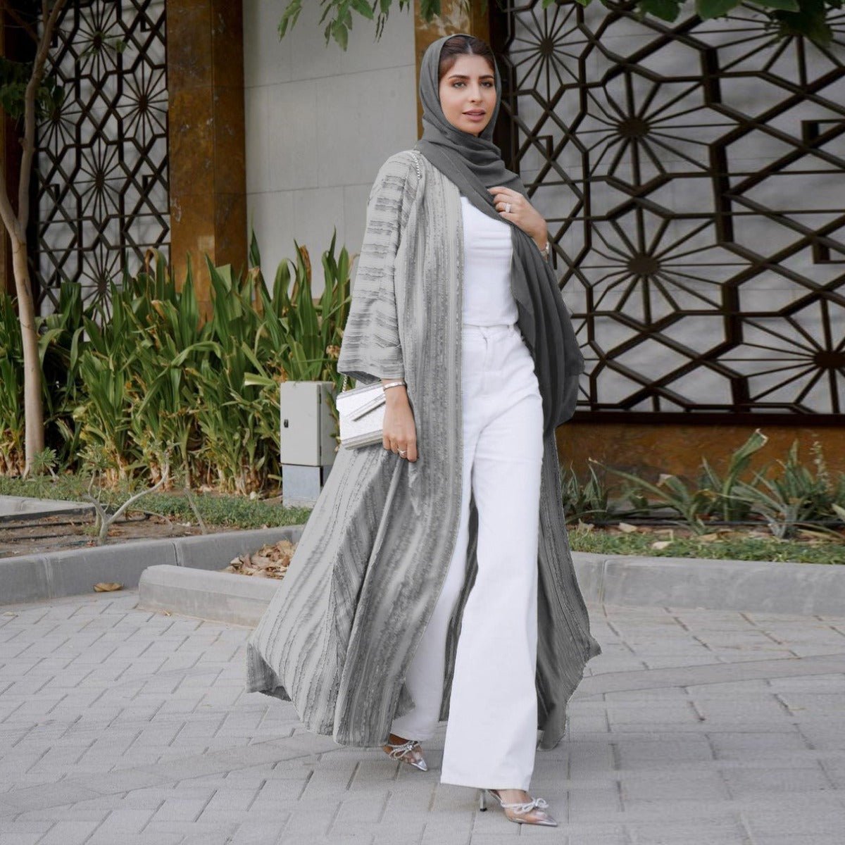 Woman wearing a grey vintage knitted longline open front cardigan abaya over white pants.